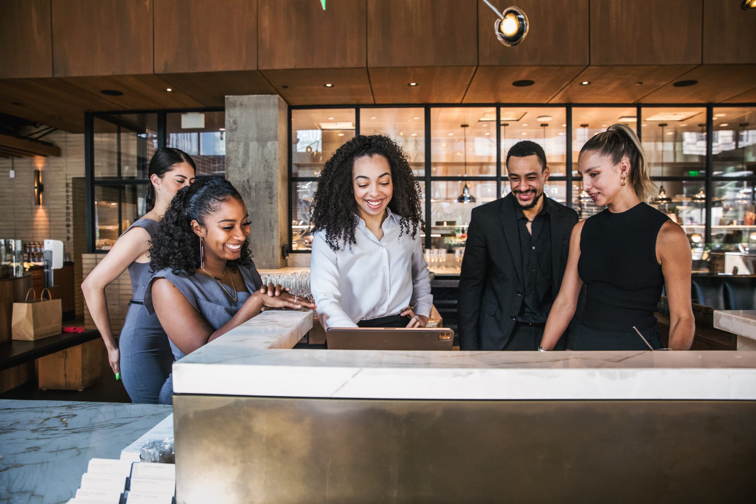 Servers and managers stood behind the hostess stand smiling looking at IPad.