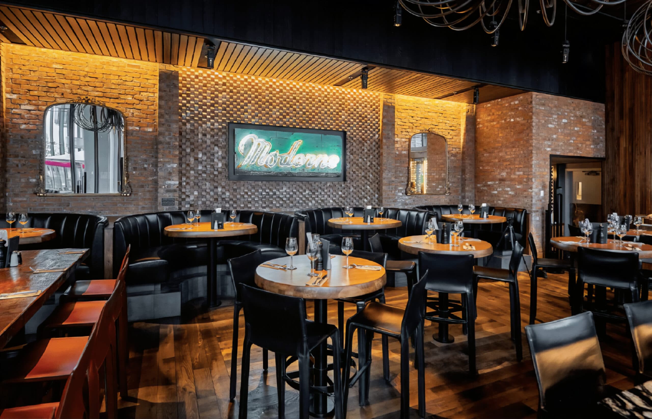 Restaurant interior with leather booths, high-top tables, ambient lighting and a neon 'Moderns' sign.