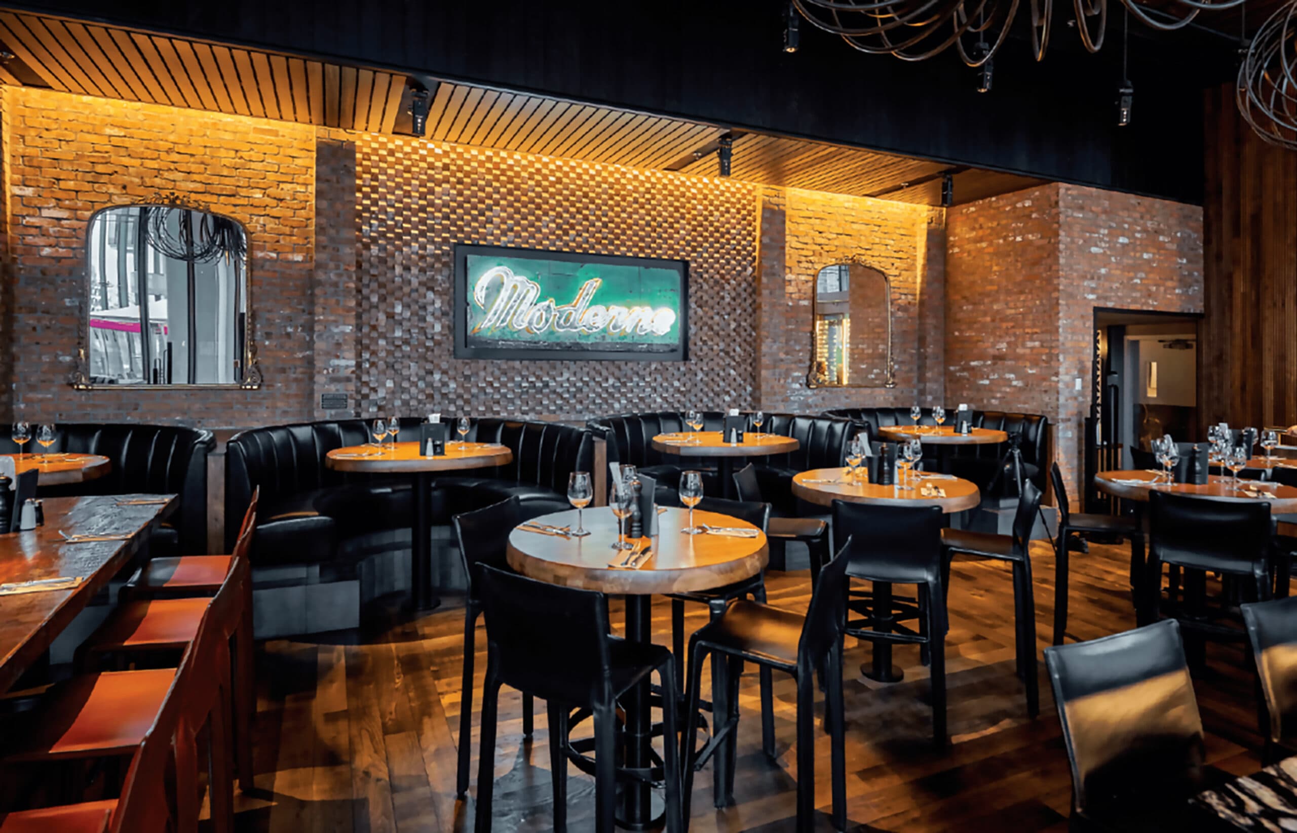 Restaurant interior with leather booths, high-top tables, ambient lighting and a neon 'Moderns' sign.